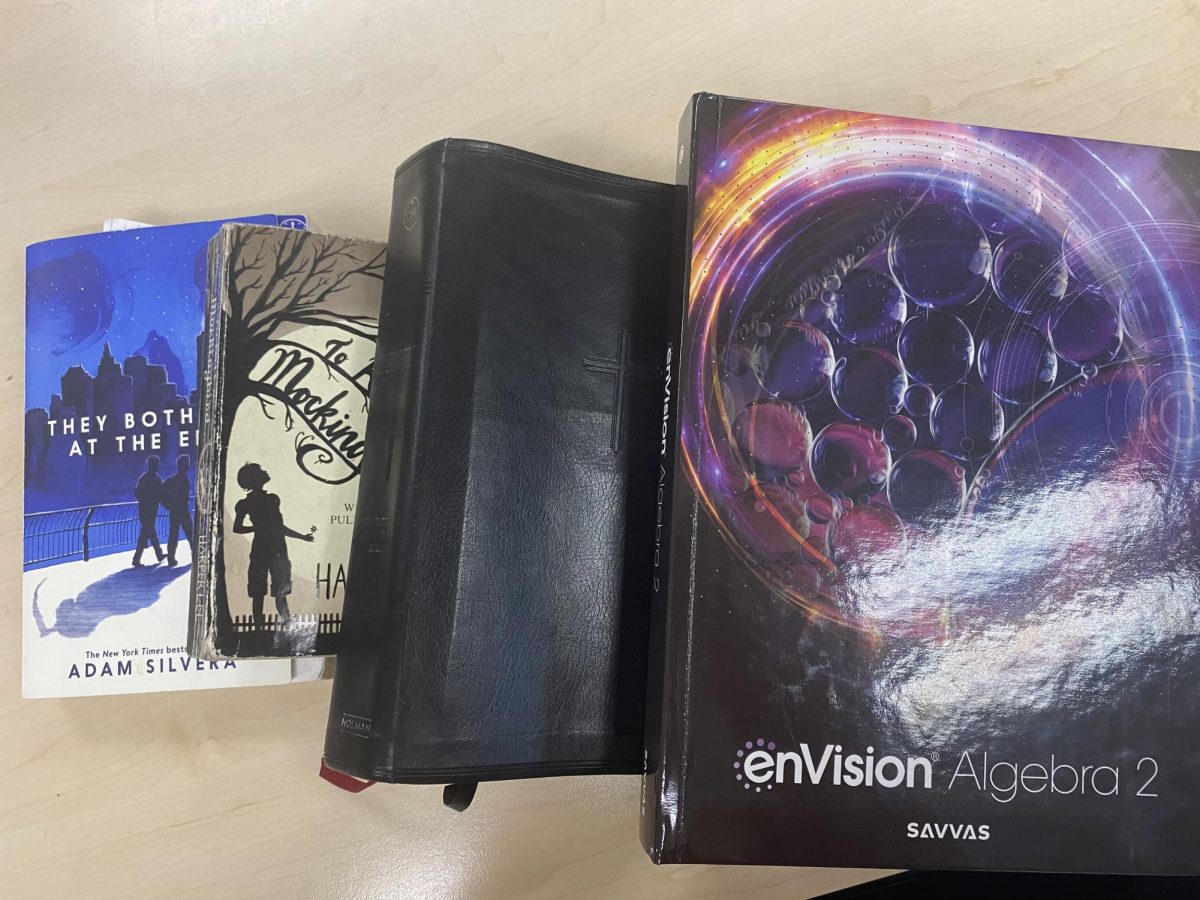 A students school books lay alongside their bible. The books are intertwined with one another rather than being separate entities. 