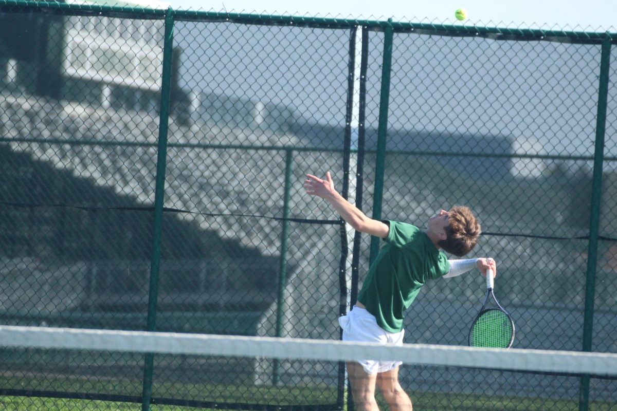 Junior Dylan Wyles serving in tennis match.